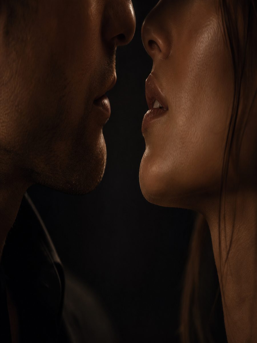 Extreme editorial crop of two lower faces inches apart in near darkness